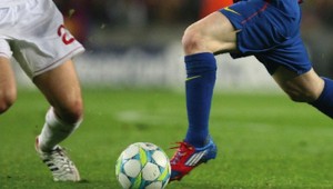 Two footballers from opposing teams about to kick a ball