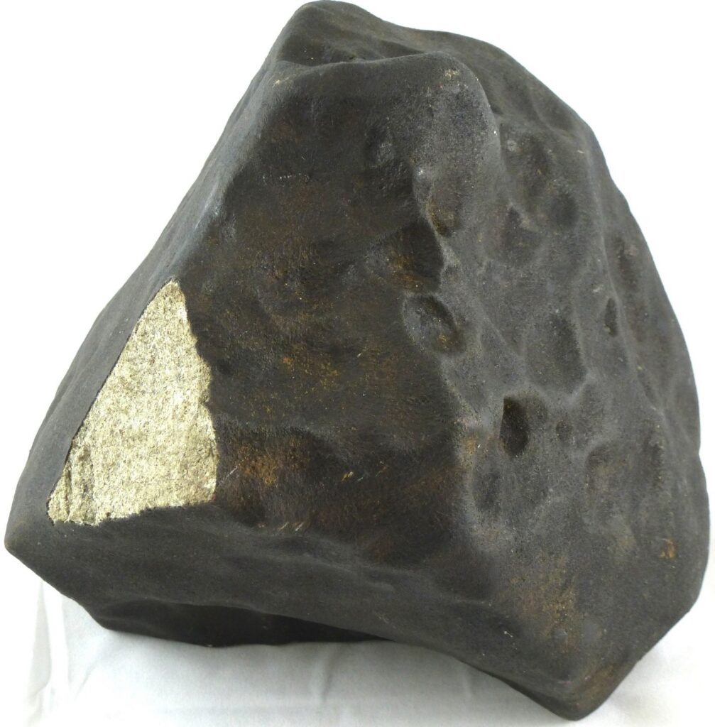 Largest specimen (6.1 kg) of the La Criolla, Argentina L6 ordinary chondrite, on display at the University of California at Los Angeles. The millimeter-thick dark fusion crust formed by melting the sample as it traversed the Earth’s atmosphere. There are shallow depressions on the surface called regmaglypts; these formed during atmospheric turbulence during descent. The light-colored, silicate-rich interior is visible at left where the fusion crust flaked off. 